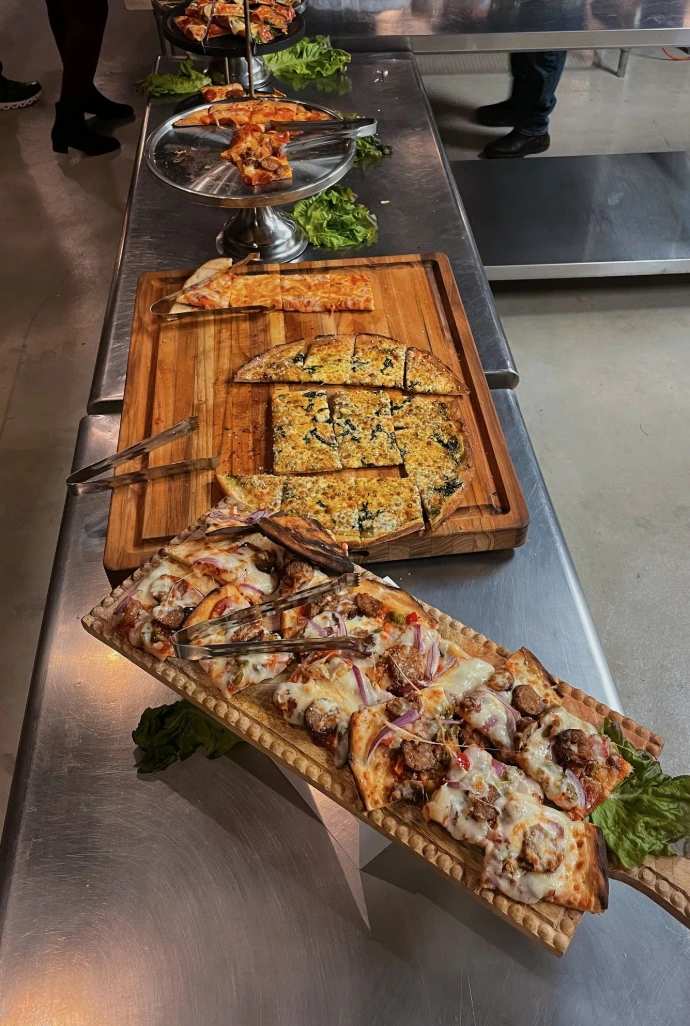 Various flavors of stone-baked pizza cut into slices and laid out on decorative wooden trays.